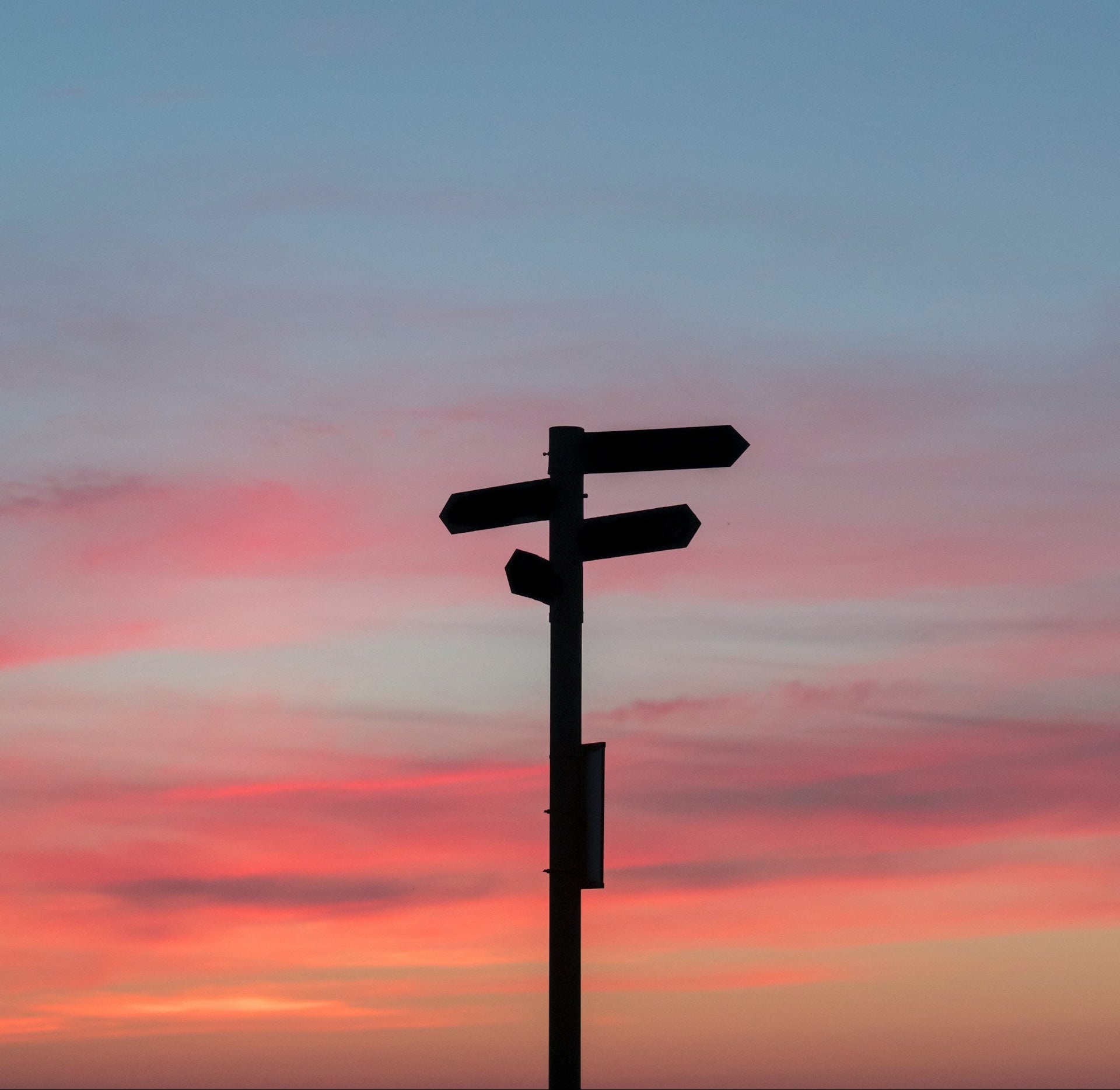Ein Wegkreuz vor einem roten Sonnenuntergang.