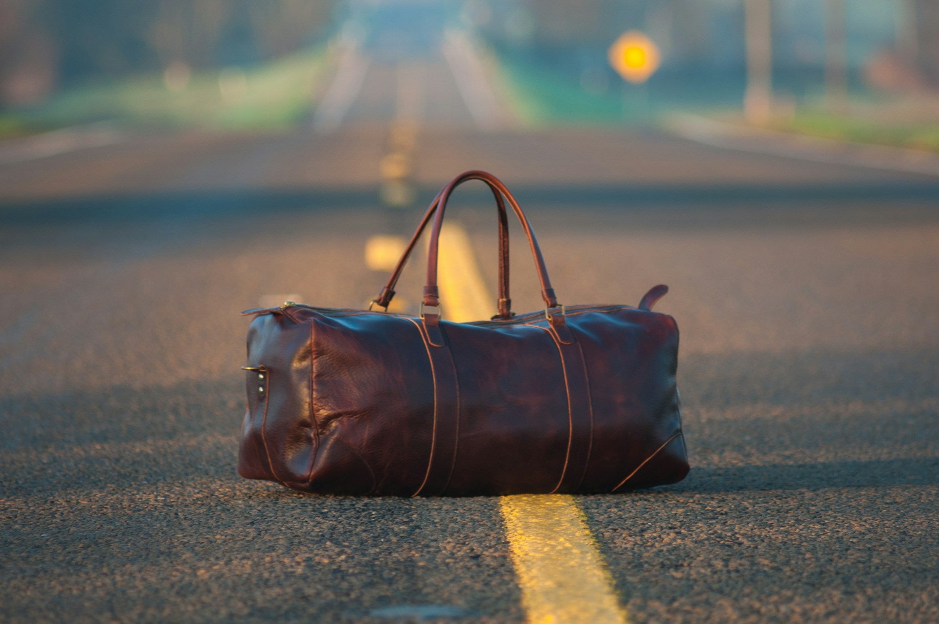 Eine Reisetasche liegt auf einem langen geraden Weg.