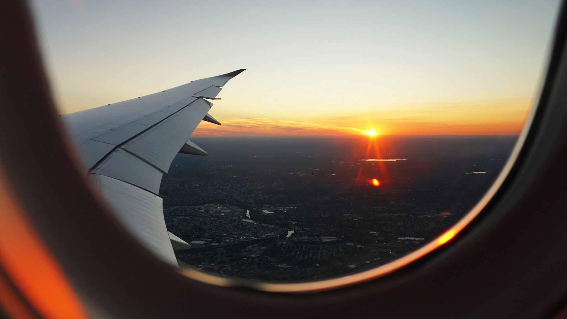 Ausblick aus einem Flugzeugfenster auf eine Stadt bei Sonnenuntergang.